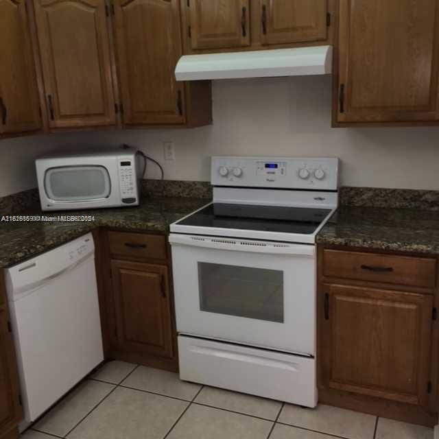 kitchen featuring dark stone counters, light tile patterned floors, ventilation hood, and white appliances