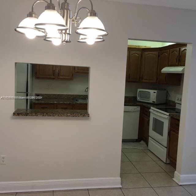 kitchen featuring white appliances, sink, hanging light fixtures, light tile patterned floors, and a chandelier