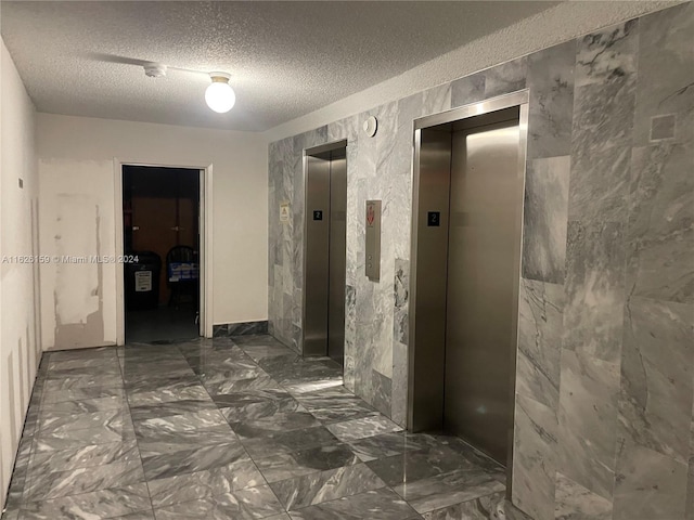 hallway with elevator, a textured ceiling, and dark tile patterned flooring