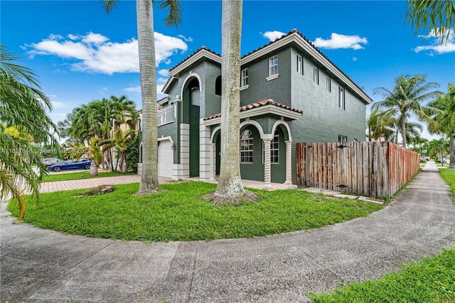 mediterranean / spanish-style house with stucco siding, decorative driveway, fence, a front yard, and a garage