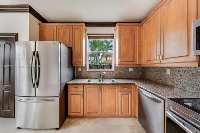 kitchen with appliances with stainless steel finishes, decorative backsplash, sink, crown molding, and light tile patterned floors