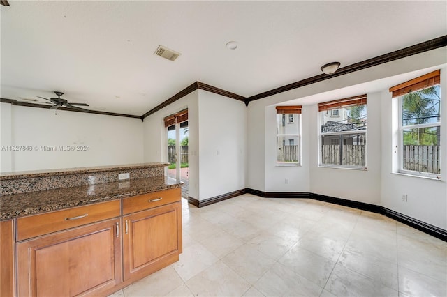 kitchen featuring ceiling fan, dark stone countertops, light tile patterned flooring, and ornamental molding