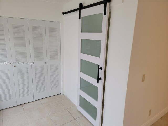 unfurnished bedroom with a barn door, light tile patterned flooring, and a closet