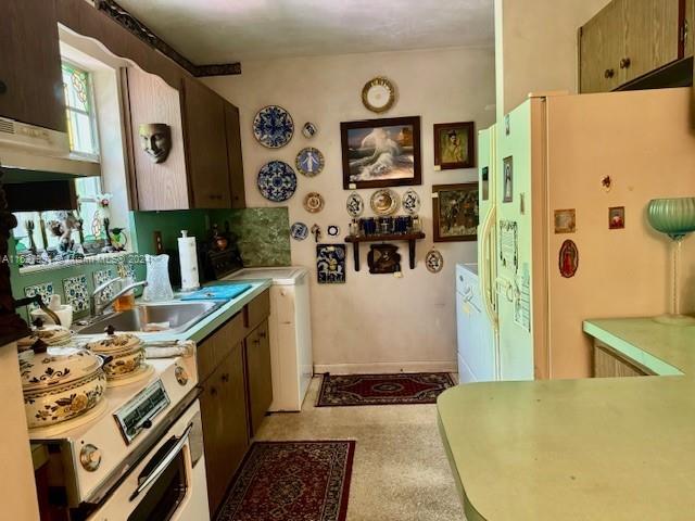 kitchen featuring washer / dryer, range, freestanding refrigerator, light countertops, and a sink