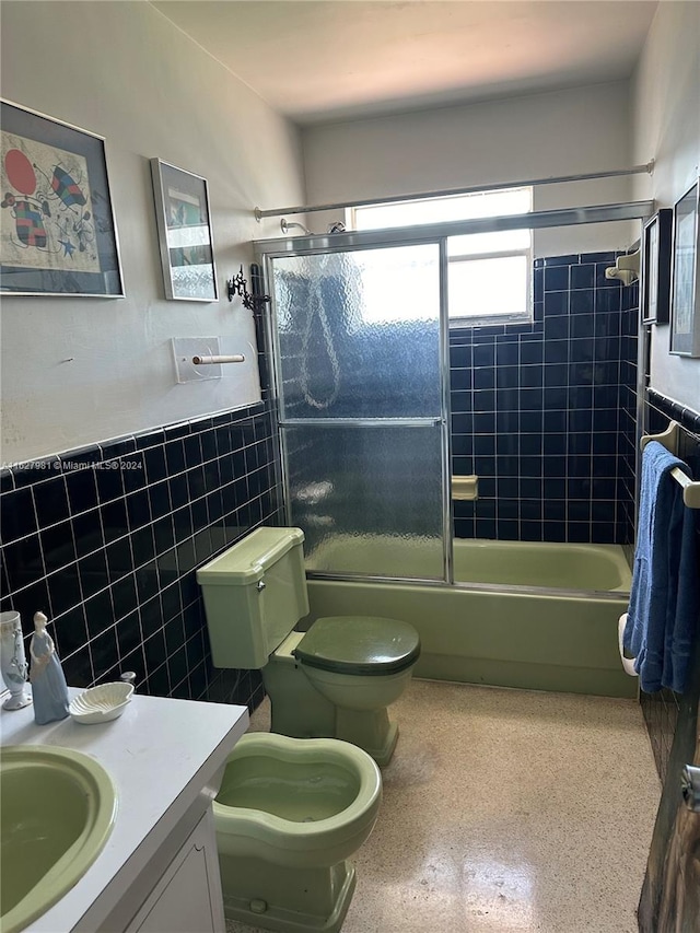 full bathroom with toilet, shower / bath combination with glass door, vanity, speckled floor, and tile walls