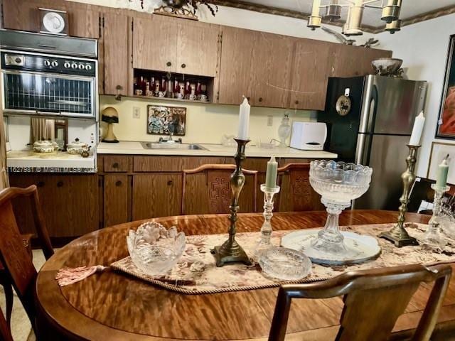 kitchen featuring double wall oven, light countertops, freestanding refrigerator, a sink, and a chandelier