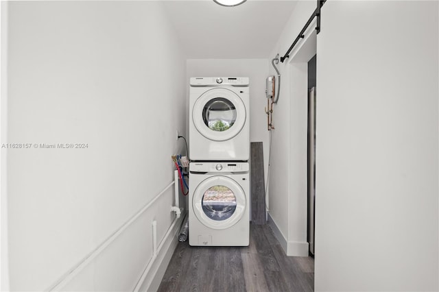 laundry area featuring stacked washer / drying machine, a barn door, and dark hardwood / wood-style flooring