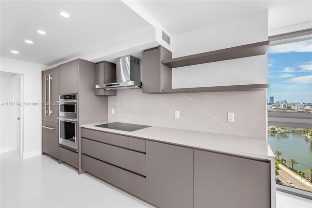 kitchen with black electric cooktop, gray cabinets, wall chimney exhaust hood, and a water view