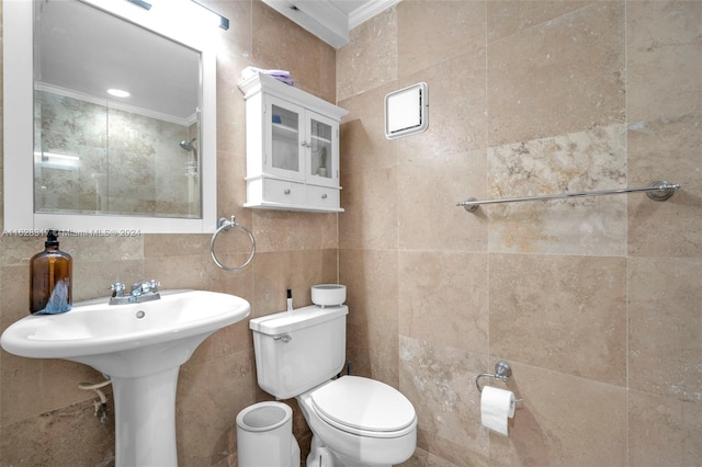 bathroom with crown molding, tile walls, toilet, a tile shower, and a sink