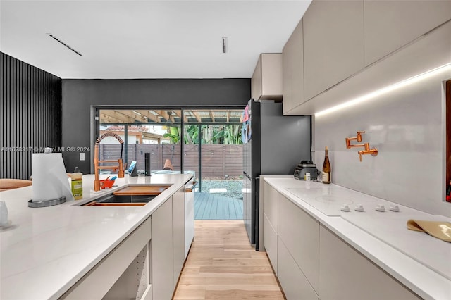 kitchen featuring light hardwood / wood-style flooring, gray cabinetry, sink, light stone counters, and black refrigerator