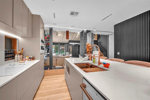 kitchen with gray cabinets, stainless steel appliances, sink, light stone countertops, and light hardwood / wood-style floors