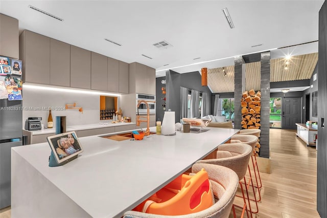 kitchen featuring a kitchen bar, a center island with sink, light wood-type flooring, and gray cabinets