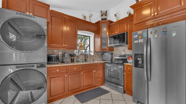 kitchen featuring light tile patterned flooring, stacked washer / dryer, stainless steel appliances, light stone countertops, and decorative backsplash