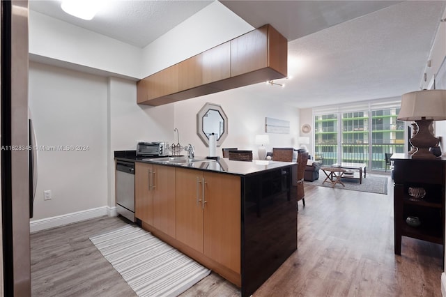 kitchen with sink, stainless steel dishwasher, a textured ceiling, and light hardwood / wood-style floors