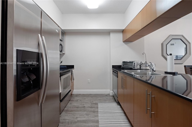 kitchen with stainless steel appliances, light hardwood / wood-style floors, sink, and dark stone countertops