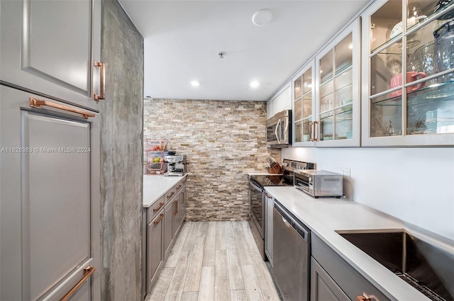 kitchen with stainless steel appliances, gray cabinets, sink, and light wood-type flooring