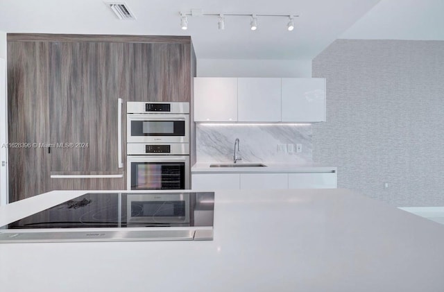 kitchen featuring double oven, white cabinetry, sink, decorative backsplash, and black electric stovetop