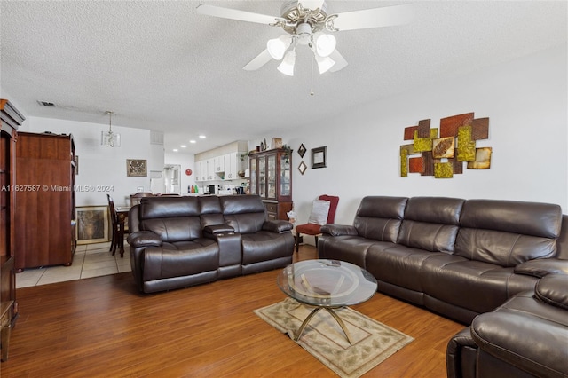 living room with ceiling fan, a textured ceiling, and light hardwood / wood-style flooring