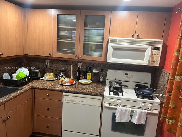 kitchen featuring dark stone countertops, decorative backsplash, and white appliances