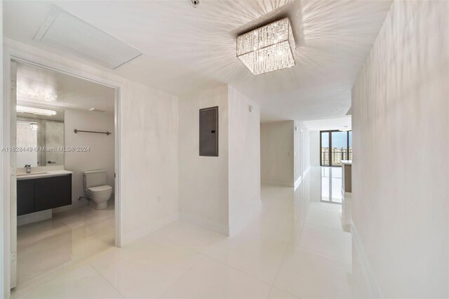 hallway featuring light tile patterned flooring, a notable chandelier, electric panel, and sink