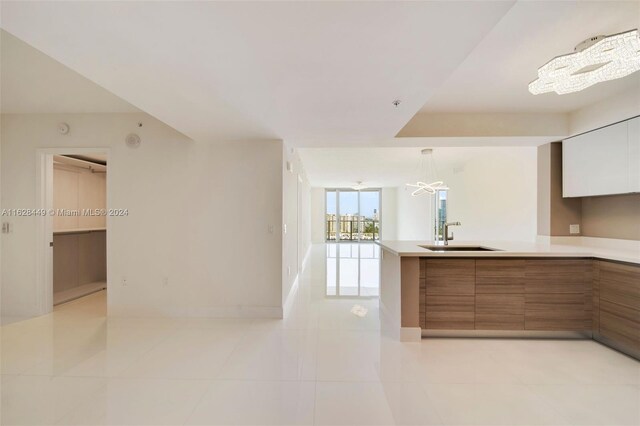 kitchen with light tile patterned flooring, white cabinets, sink, kitchen peninsula, and decorative light fixtures