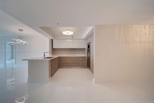 kitchen with pendant lighting, white cabinets, light tile patterned floors, sink, and kitchen peninsula