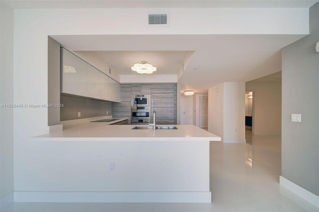 kitchen with double oven, black electric cooktop, light tile patterned floors, sink, and kitchen peninsula