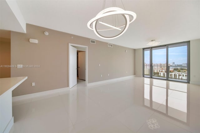 tiled spare room featuring an inviting chandelier and expansive windows