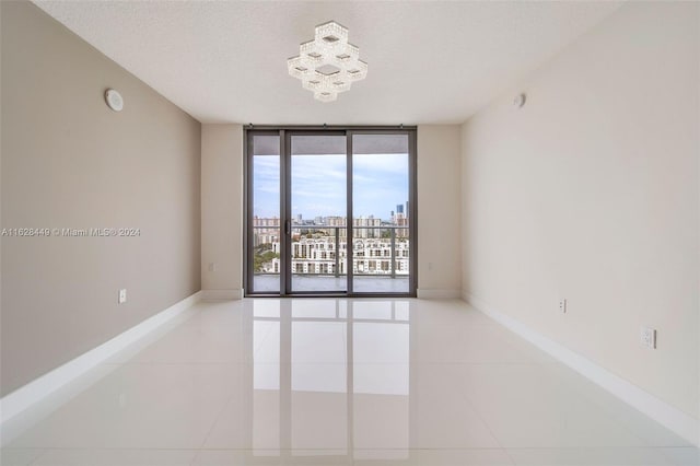 tiled spare room with a textured ceiling, a wall of windows, and a chandelier