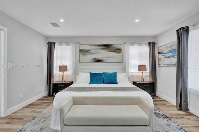 bedroom with multiple windows, a textured ceiling, and light wood-type flooring