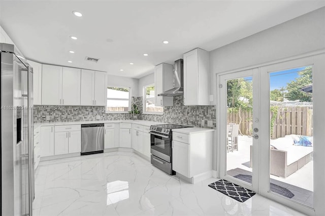 kitchen featuring white cabinets, appliances with stainless steel finishes, wall chimney exhaust hood, and french doors