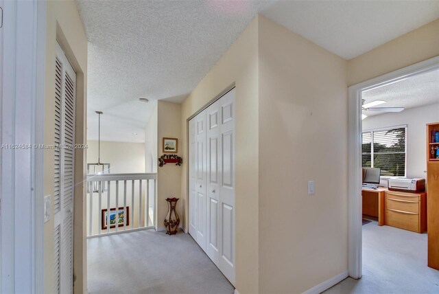 corridor with a textured ceiling and light colored carpet