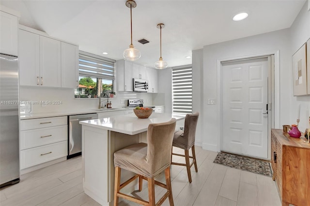 kitchen with pendant lighting, stainless steel appliances, a center island, and white cabinets