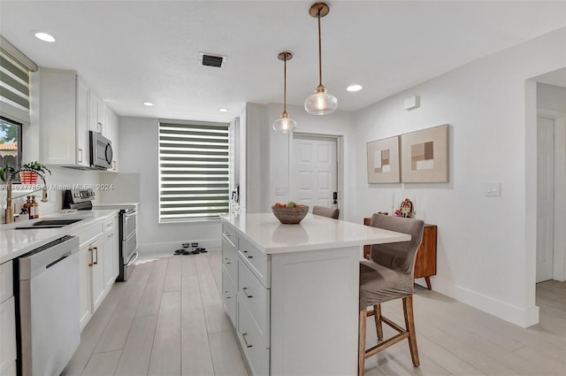 kitchen featuring decorative light fixtures, white cabinetry, sink, a center island, and stainless steel appliances