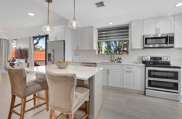 kitchen with sink, white cabinetry, stainless steel appliances, a kitchen breakfast bar, and decorative light fixtures