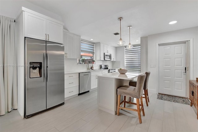 kitchen with a breakfast bar area, appliances with stainless steel finishes, white cabinetry, a kitchen island, and decorative light fixtures