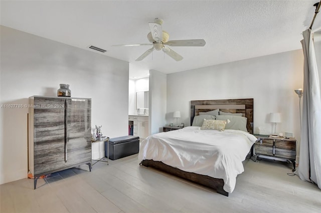 bedroom featuring ceiling fan, ensuite bath, light hardwood / wood-style floors, and a textured ceiling