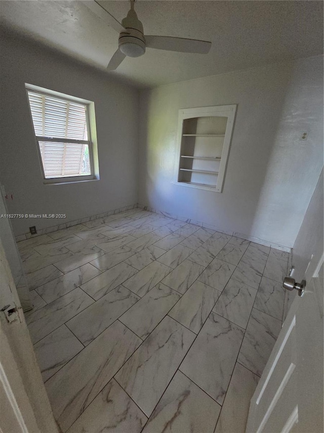 spare room with a ceiling fan, marble finish floor, and built in features