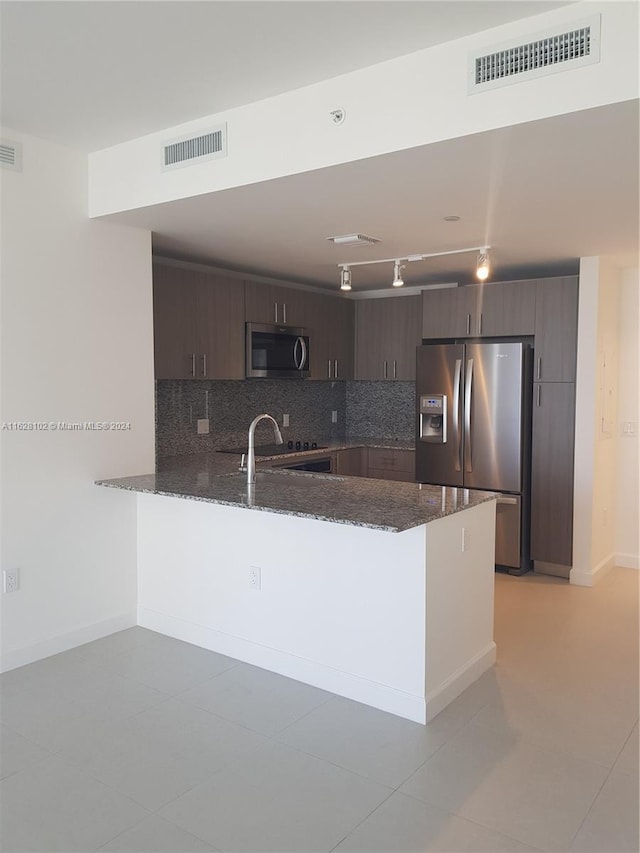 kitchen featuring kitchen peninsula, appliances with stainless steel finishes, tasteful backsplash, dark stone counters, and dark brown cabinetry