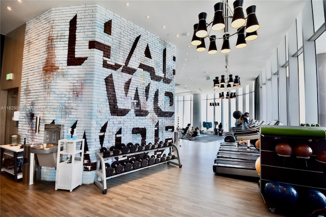 exercise room with brick wall, a notable chandelier, and hardwood / wood-style floors