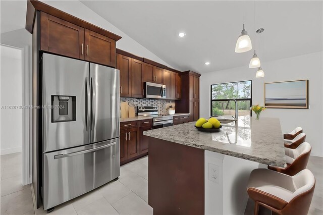 kitchen featuring a breakfast bar area, light stone counters, vaulted ceiling, stainless steel appliances, and a kitchen island with sink