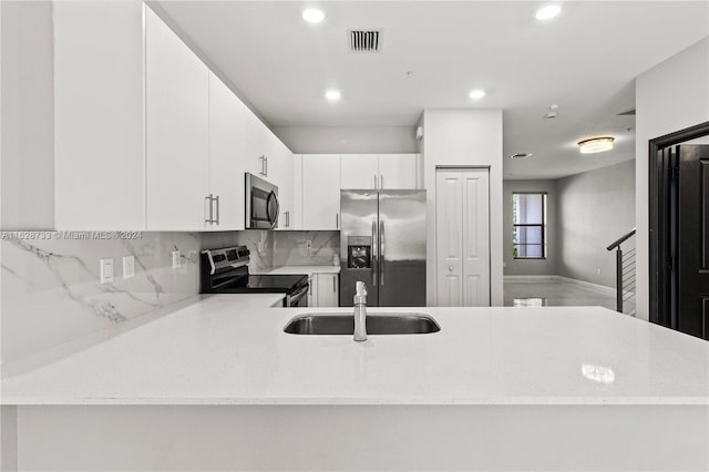 kitchen featuring sink, kitchen peninsula, tasteful backsplash, white cabinetry, and stainless steel appliances