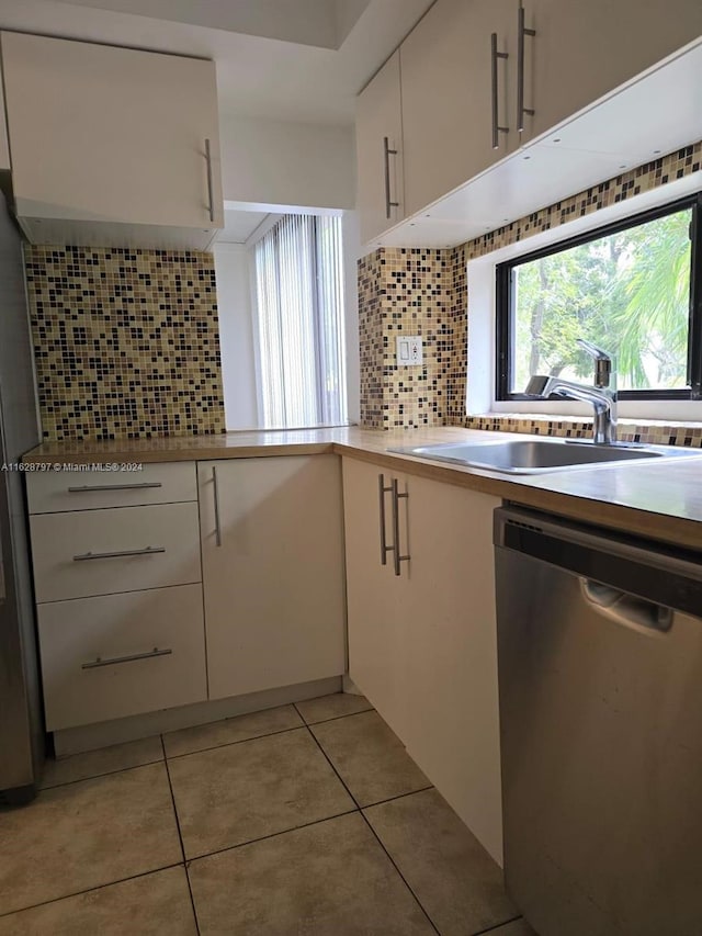 kitchen featuring white cabinetry, sink, stainless steel dishwasher, decorative backsplash, and light tile patterned flooring