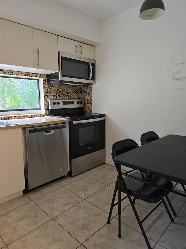 kitchen featuring decorative backsplash, white cabinets, light tile patterned floors, and appliances with stainless steel finishes