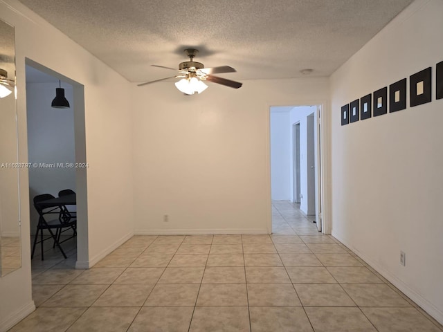 empty room with ceiling fan, light tile patterned floors, and a textured ceiling