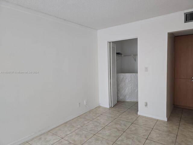 unfurnished bedroom with a walk in closet, a textured ceiling, light tile patterned floors, and a closet