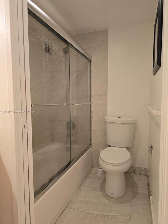 bathroom featuring tile patterned flooring, combined bath / shower with glass door, and toilet