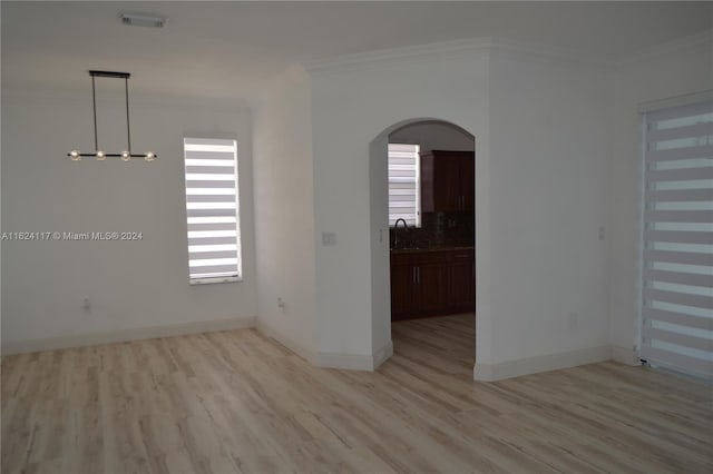 spare room featuring sink, crown molding, light wood-type flooring, and a chandelier