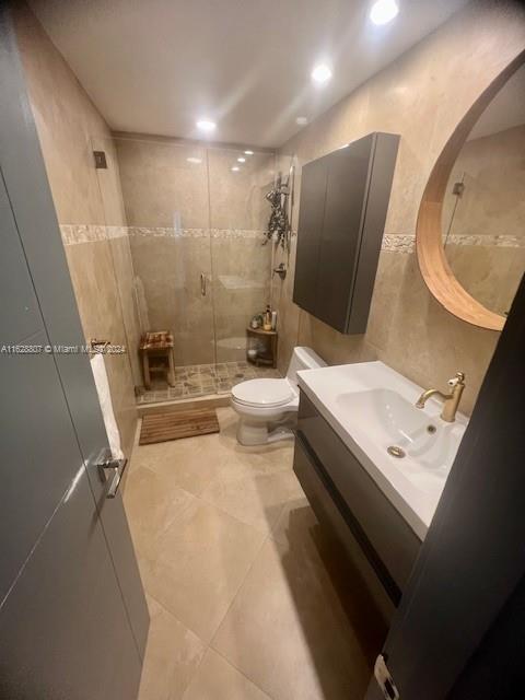 bathroom featuring tile walls, vanity, toilet, a shower with door, and tile patterned floors