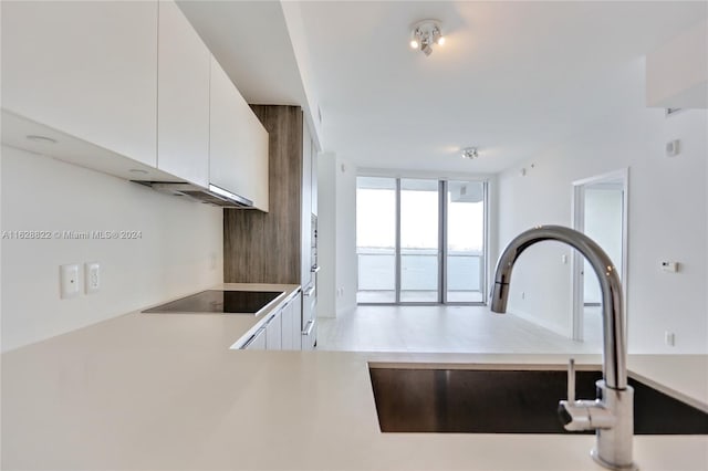 kitchen with white cabinets, black electric cooktop, expansive windows, and sink